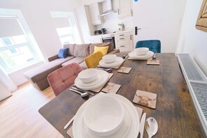 A dining table set with plates, bowls, and cutlery, a sofa, and a kitchen in the background. - Modern Apartments in Central Derry I Each Apartment Sleeps 4 (Derry/Londonderry)