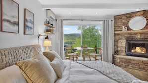 Un dormitorio con cama, chimenea, una mesa de comedor con sillas y vista a zonas verdes.