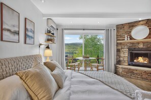 Una camera da letto con un letto, un camino, un tavolo da pranzo con sedie e vista sul verde circostante.