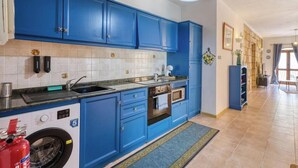 A kitchen with blue cabinets, a washing machine, a microwave, and a dining area with a table and chairs. - St. Julian`s 1BR home w/ Fast Wi-Fi & Comfy Bed (St. Julian`s)