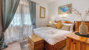A bedroom with a wooden bed, a nightstand, a bedside table, a woven vase, and a painting on the wall. - St. Julian`s 1BR home w/ Fast Wi-Fi & Comfy Bed (St. Julian`s)