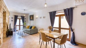 A living room with a sofa, a dining table with chairs, a TV, and a window with curtains. - St. Julian`s 1BR home w/ Fast Wi-Fi & Comfy Bed (St. Julian`s)