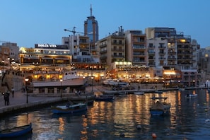 A waterfront cityscape with a prominent building labeled 'DOLCE VITA' and a marina with boats. - St. Julian`s 1BR home w/ Fast Wi-Fi & Comfy Bed (St. Julian`s)