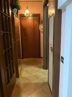Um corredor com uma porta de madeira, uma porta de vidro com grade de metal e um chão de azulejos.