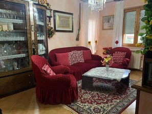 Uma sala de estar com um sofá vermelho, uma mesa de centro, um aparador de vidro e um candelabro.
