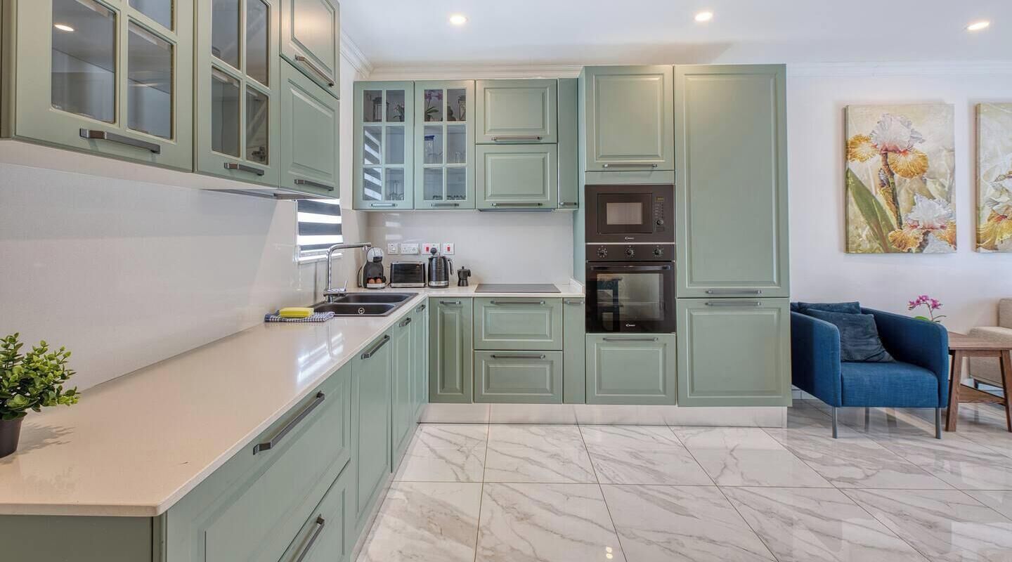 Une cuisine moderne avec des meubles de couleur vert clair, un sol en marbre et un canapé bleu dans l’espace salon.
