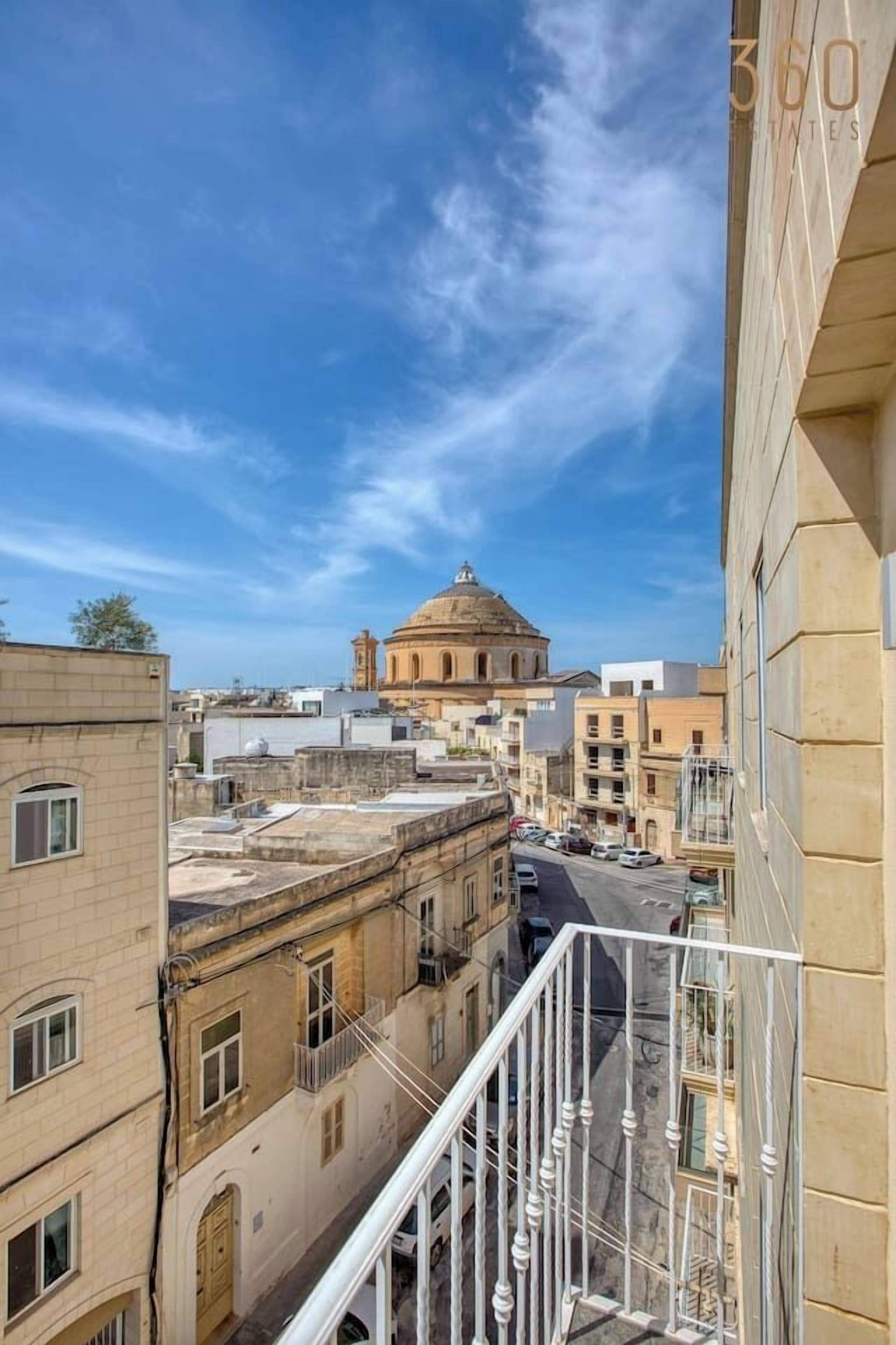 A view from a balcony overlooking a city street with a historic building in the background.