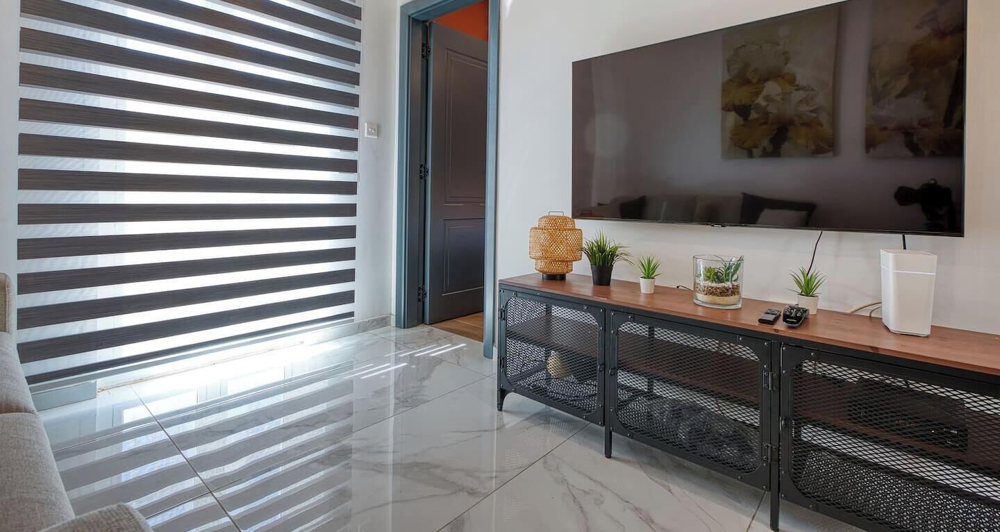 A modern living room with a large TV, a console table with plants, and a sliding door with blinds.