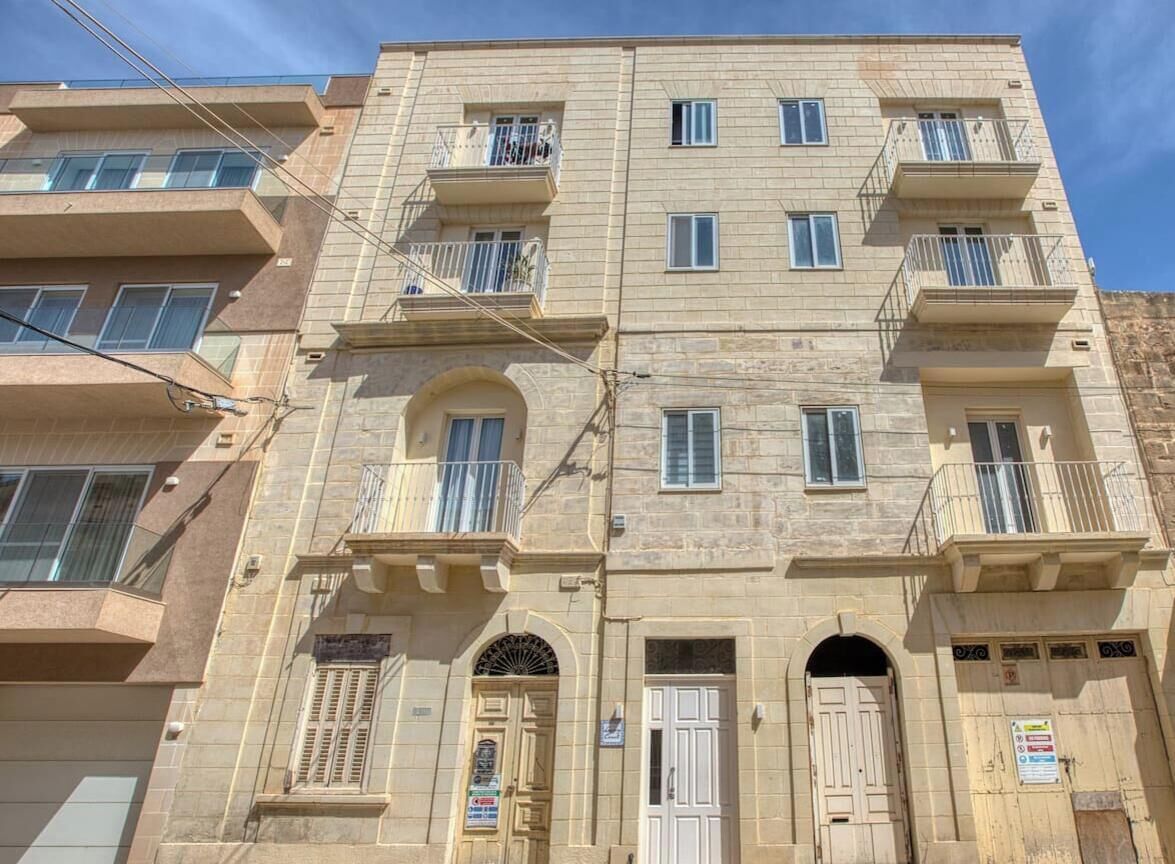 A multi-story building with balconies, arched doorways, and a signboard.