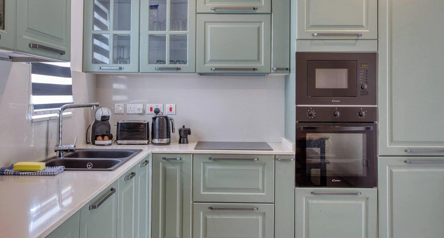 Una cocina con gabinetes verde claro, un fregadero de acero inoxidable, una cafetera y un horno empotrado.