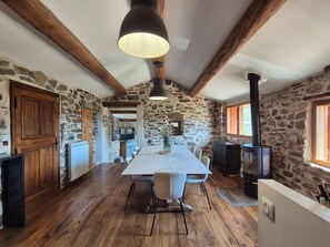 Une cuisine rustique avec des murs en pierre, des poutres en bois, une grande table et un poêle à bois.