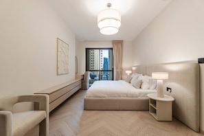 A modern hotel room with a large bed, a desk, a chair, a bedside table with a lamp, and a view of the cityscape. - Stylish Renovated 1BR At Prime JBR Location (Dubai)