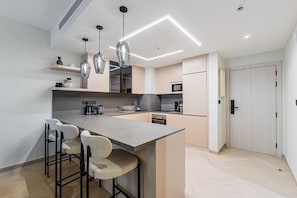 A modern kitchen with a central island, bar stools, pendant lighting, and a microwave. - Stylish Renovated 1BR At Prime JBR Location (Dubai)