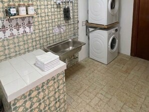 A kitchen with a sink, stacked towels, a washing machine, and patterned tiles. - Charming Holiday House in Almazora (Almassora)