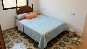 A single bed with a blue bedspread and a wooden headboard, a small window with blinds, and patterned floor tiles. - Charming Holiday House in Almazora (Almassora)