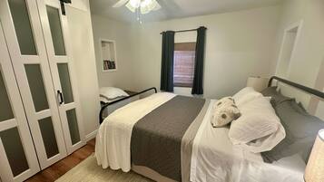 Un dormitorio con una cama, una mesita de noche, un ventilador de techo y una ventana con cortinas.