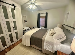 A bedroom with a bed, a bedside table, a ceiling fan, and a window with curtains.