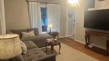Una sala de estar con un sofá, una mesa de centro, una lámpara, un televisor y una puerta con cortinas.