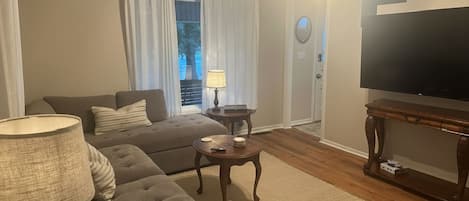 A living room with a sofa, a coffee table, a lamp, a television, and a door with curtains.