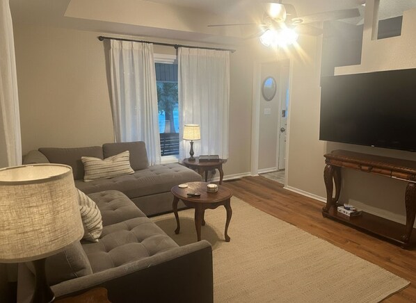A living room with a sofa, a coffee table, a lamp, a television, and a door with curtains.