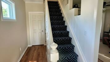 Una escalera con un estampado de zigzag en la alfombra, una puerta blanca en la parte superior y una ventana a la izquierda.