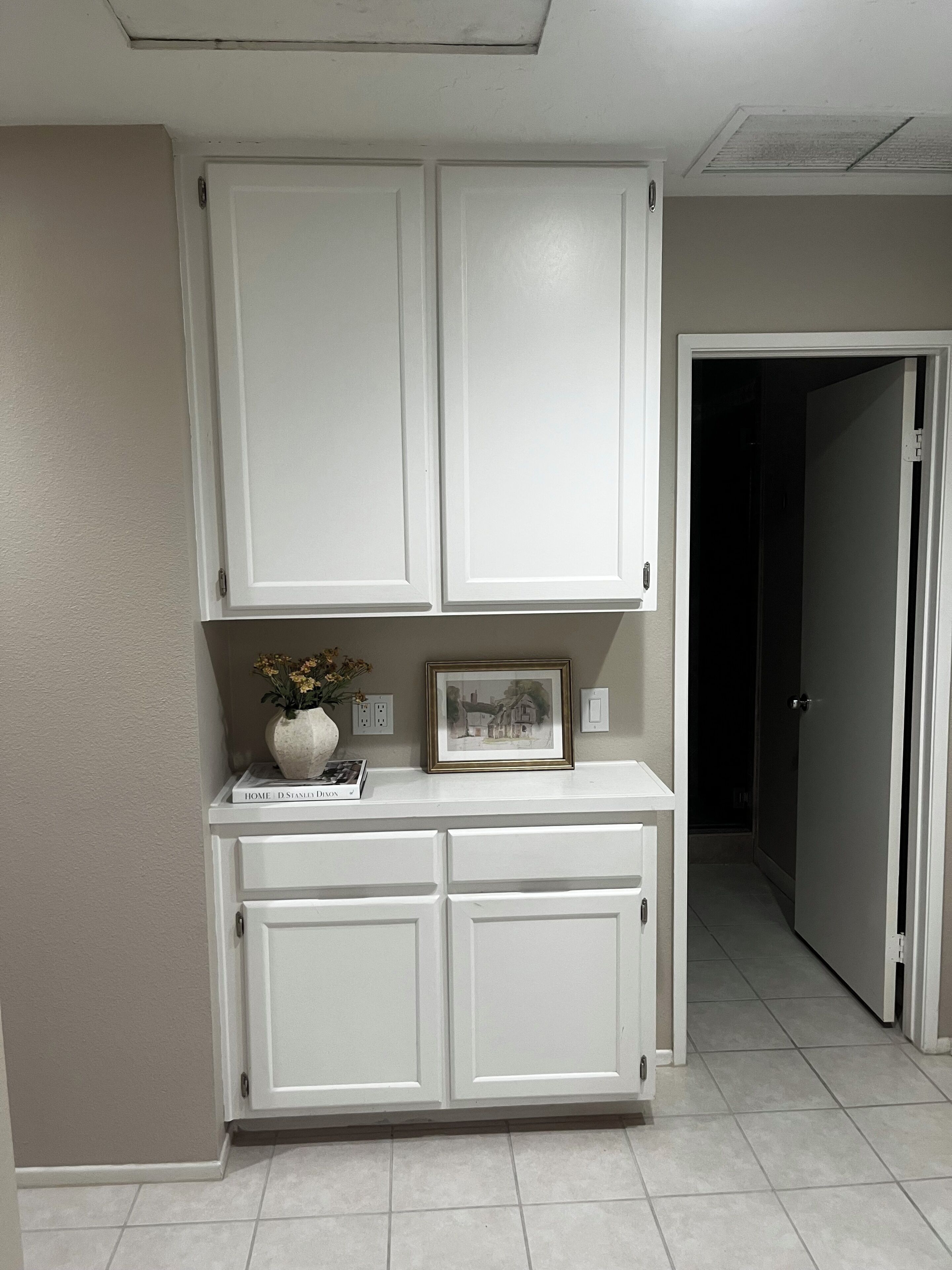 A hallway with a white door, a white cabinet with a vase and a framed picture, and a book titled 'HOME' by D. STANLEY DYSON.
