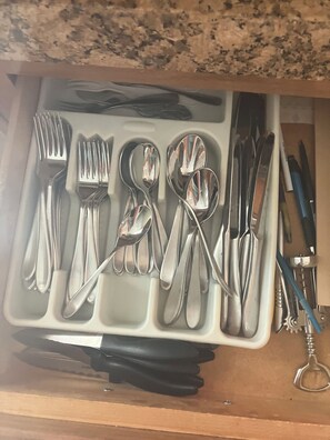 Eine Schublade mit verschiedenen Besteckstücken, darunter Gabeln, Löffel und Messer, sowie einem Schlüsselbund.