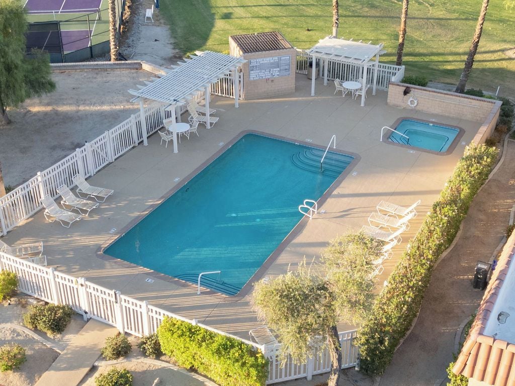 An outdoor swimming pool with a deck, lounge chairs, and a small pavilion.