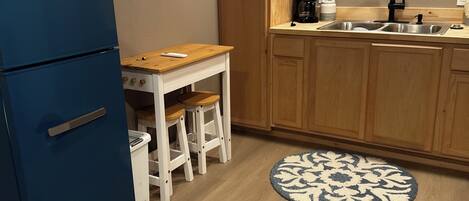 A compact kitchen with a blue refrigerator, wooden cabinets, a sink, and a round rug.