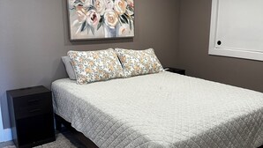 Um quarto com uma cama, uma mesa de cabeceira, um quadro e uma janela.