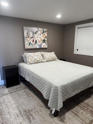 A bedroom with a bed, a nightstand, a painting, and a window. - Cozy 1-bedroom barndo in brilliant Orange City with AC (Orange City)