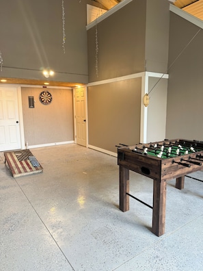 Une pièce avec une table de baby-foot, un jeu de fléchettes et un petit drapeau américain posé sur le sol, à titre décoratif.
