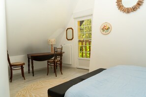 Une chambre à coucher comprenant un lit, un bureau avec une chaise, une fenêtre donnant sur un espace verdoyant et un miroir fixé au mur.