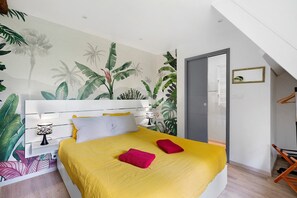 Et moderne soveværelse med en seng, et natbord, en lampe og et vægmaleri med et tropisk tema.