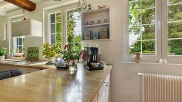 A kitchen with a wooden countertop, a coffee machine, and a window with a view of trees.