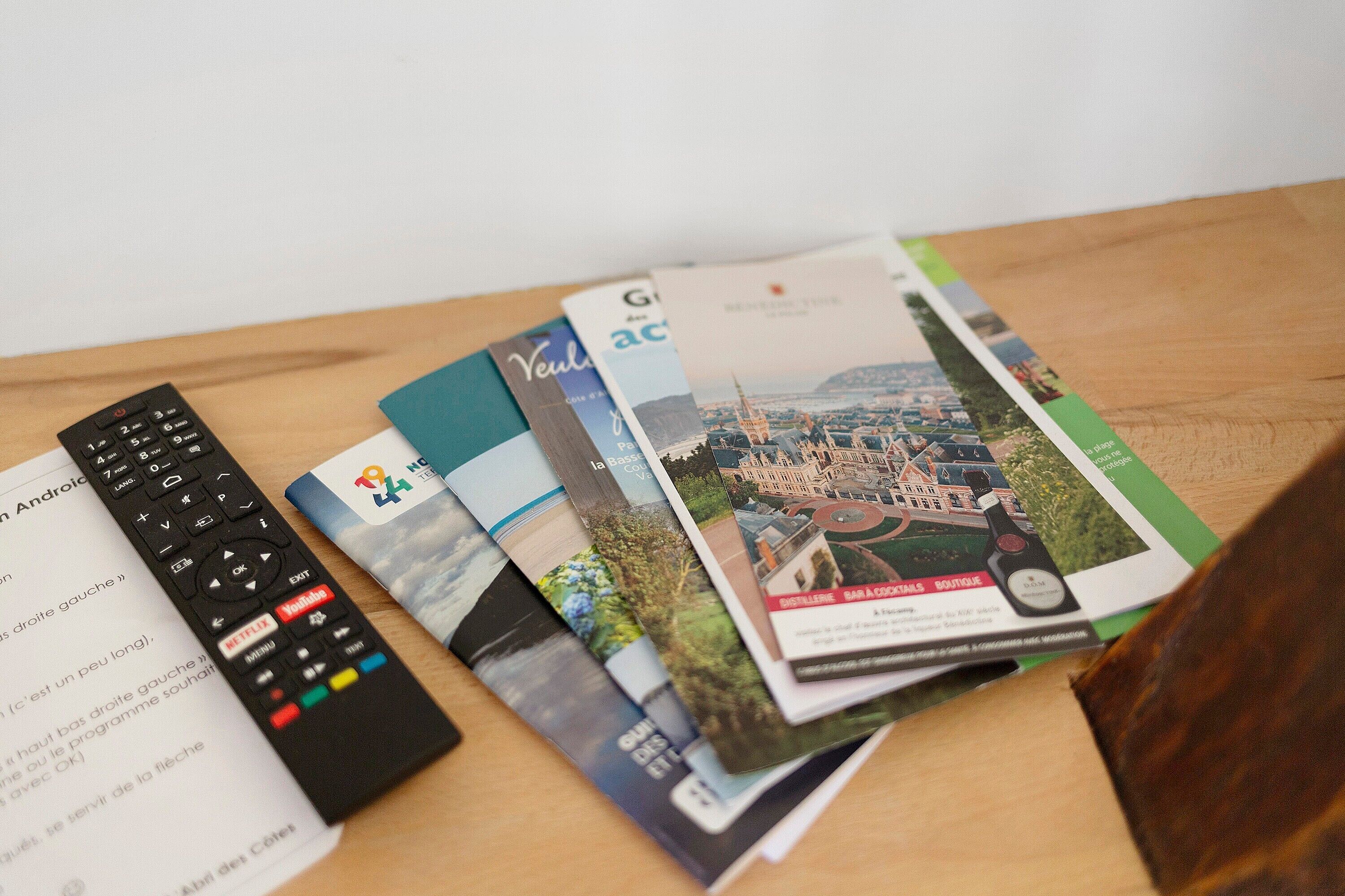 Une télécommande, un manuel d’utilisation et un magazine, posés sur une surface en bois.