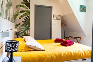 Ein Schlafzimmer mit gelber Bettdecke, einer grauen Tür, einem Spiegel und einer Wand aus Pflanzen.