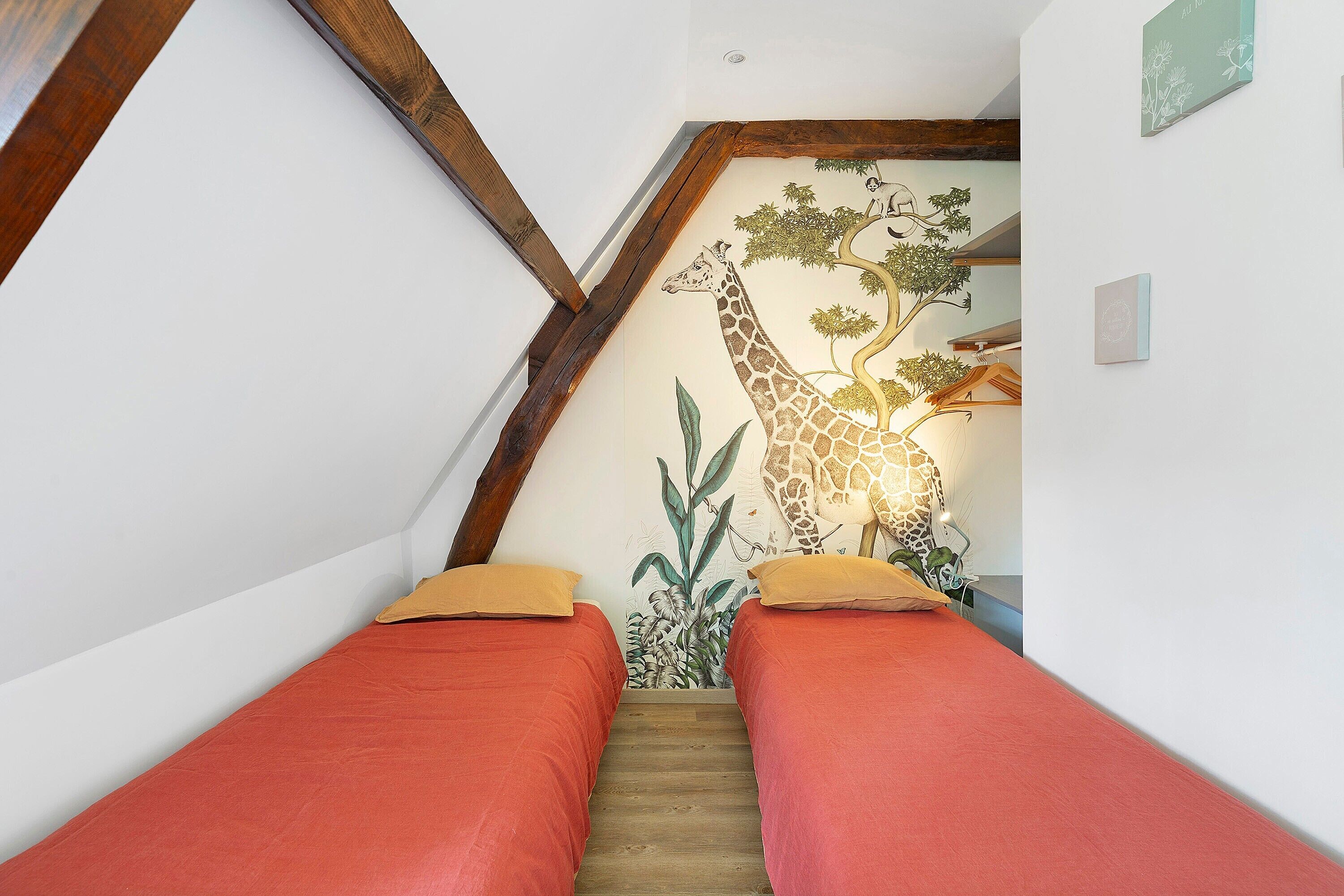 Une chambre avec un plafond en pente, une fresque représentant une girafe et deux lits avec une literie rouge.
