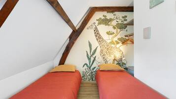A bedroom with a sloped ceiling, a giraffe mural, and two beds with red bedding.