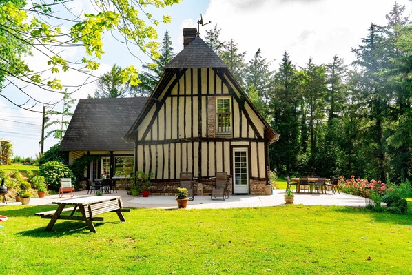 Ein traditionelles Fachwerkhäuschen mit einem geneigten Dach, einer Veranda mit Sitzgelegenheiten und einem gepflegten Garten.