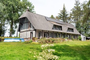 Ein großes, zweistöckiges Haus mit einem steilen Satteldach, umgeben von einem gepflegten Rasen und Bäumen.