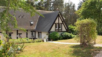 Una casa tradizionale a graticcio con tetto spiovente, circondata da un giardino curato e alberi.
