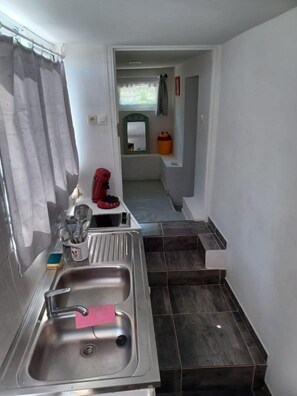 Eine Küche mit einem Edelstahl-Spülbecken, einem roten Wasserkocher und einer kleinen Arbeitsplatte mit Küchenutensilien.