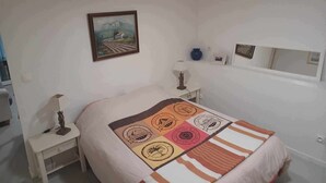 A bedroom with a bed, a nightstand, a lamp, a painting, and a mirror. - Apartment with pool and garden (Boisset-et-Gaujac)
