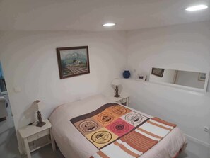 Ein Schlafzimmer mit Bett, Nachttisch, Lampe, Gemälde und Spiegel.