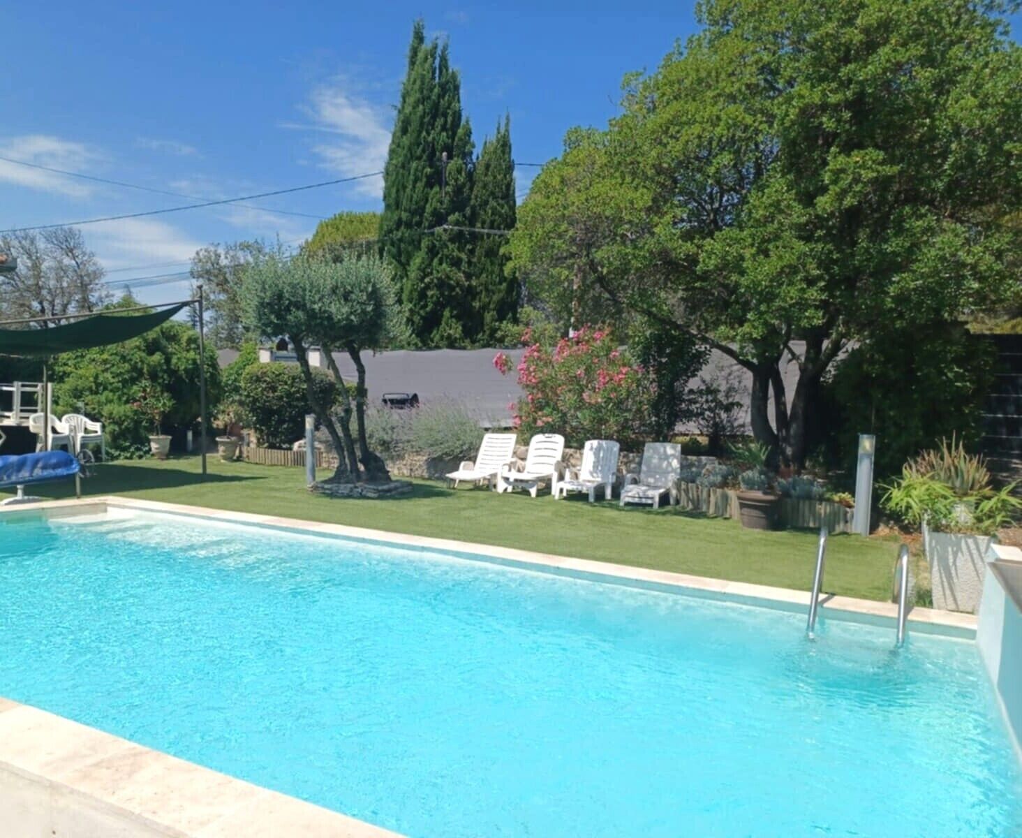 A swimming pool with lounge chairs, a covered seating area, and a garden with trees and shrubs.
