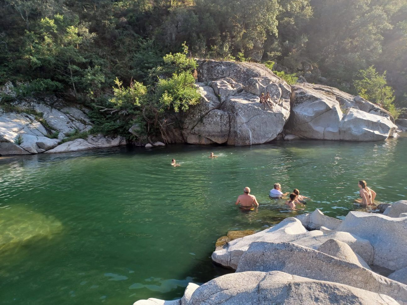 A natural pool surrounded by large rocks and greenery.