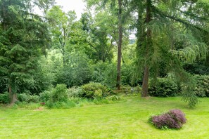 Un jardí exuberant amb diverses plantes i arbustos, una petita zona d'estar amb cadires, i un pràctic gresol.