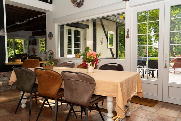 A dining area with a table set for four, chairs, a vase with flowers, and a view through the window.