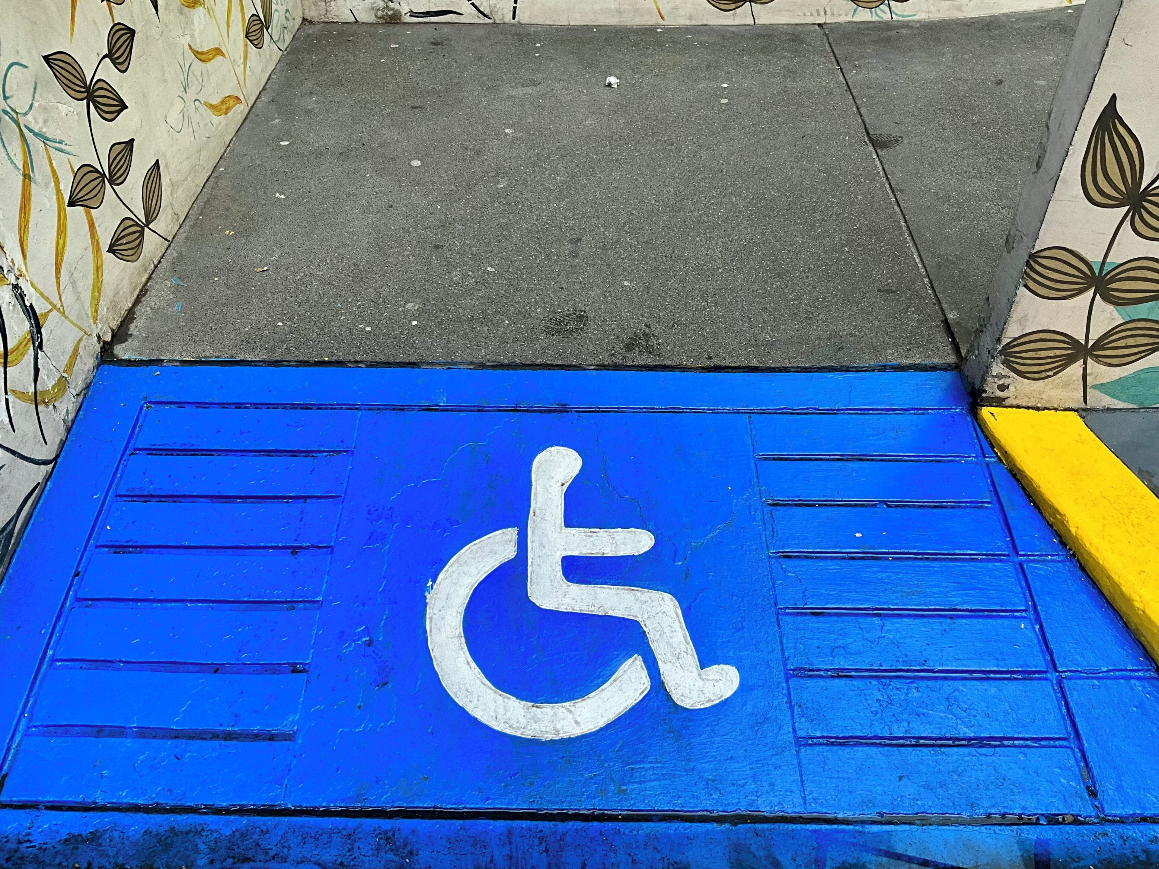 Une rampe bleue, agréée pour l’accès aux personnes en fauteuil roulant, mène à l’entrée d’un bâtiment.
